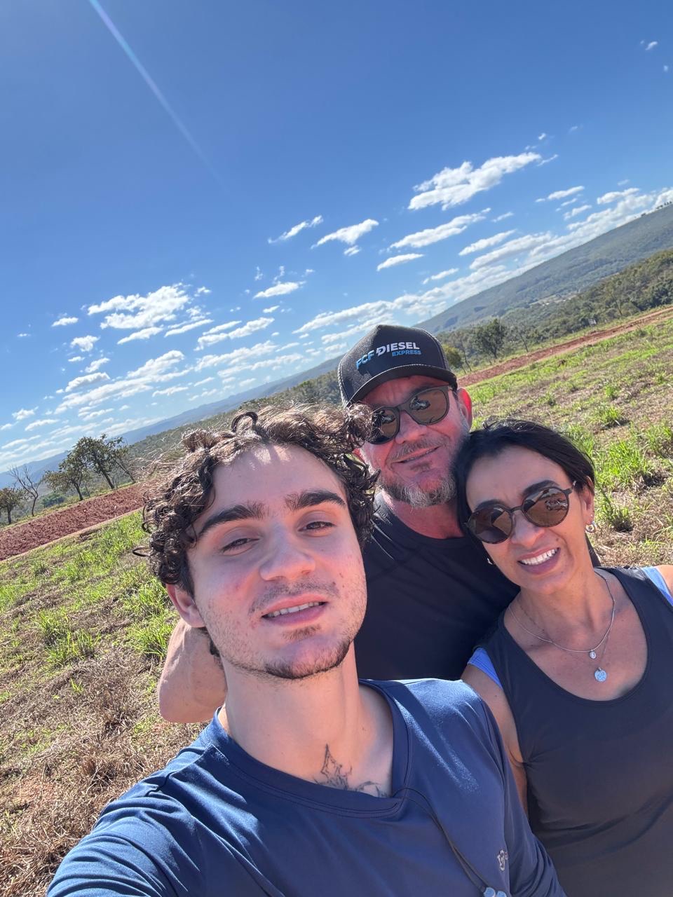 Dani com a esposa Giupira e o filho Felipe, selfie num campo aberto sob o céu azul.