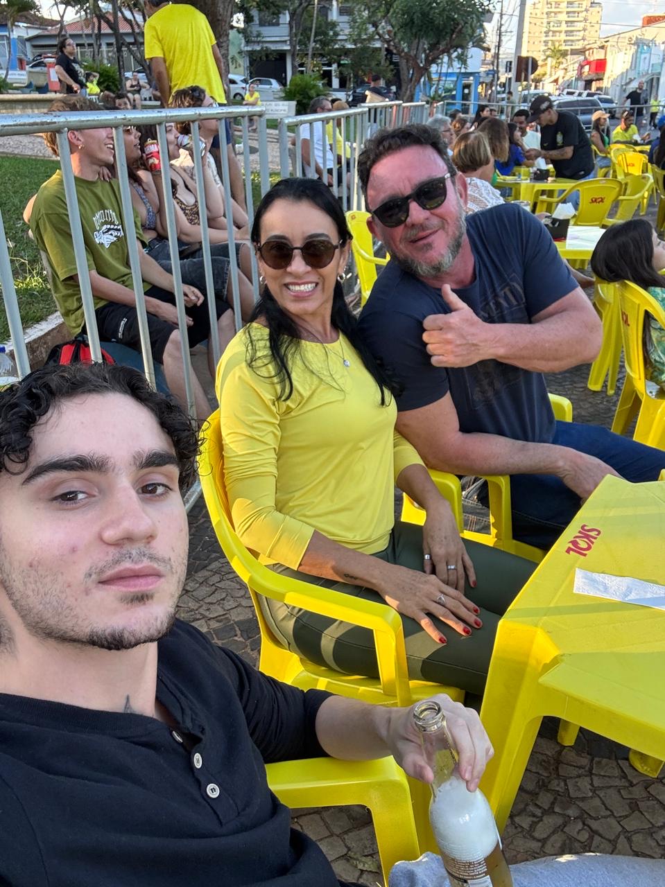Dani, Giupira e Felipe sentados juntos numa praça, clima de festa.