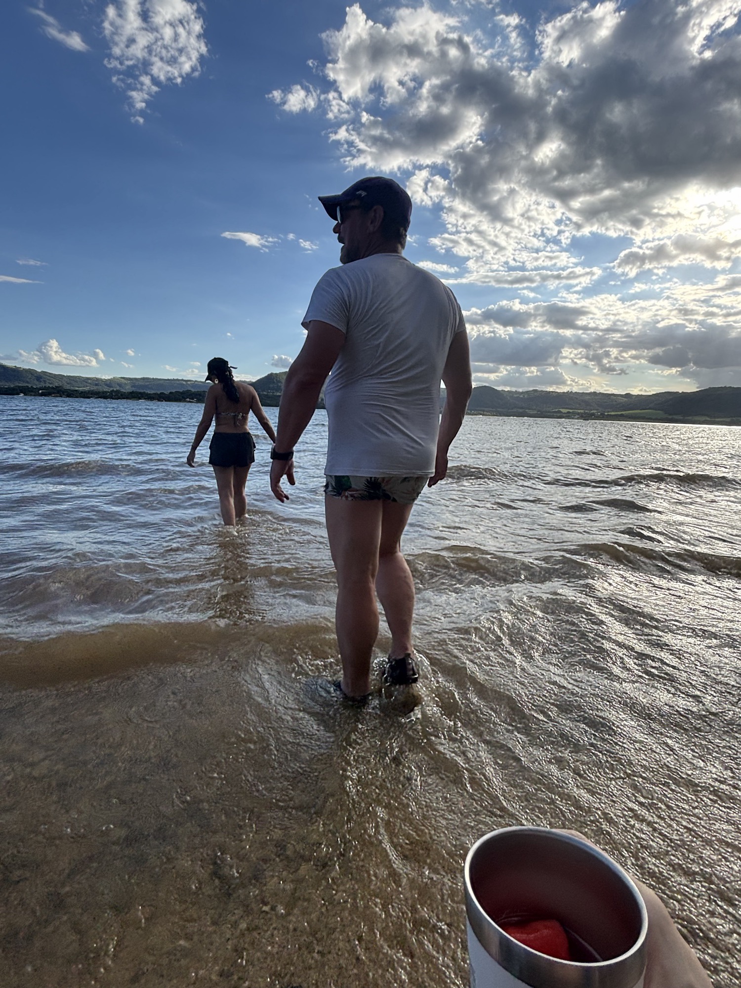 Daniel e Giupira caminhando de mãos dadas dentro d'água, ao entardecer, na represa de Rifaina.