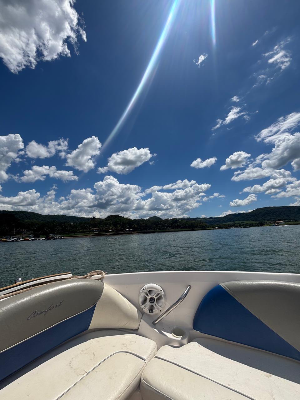 Proa de uma lancha na represa, sol estourando no céu azul.